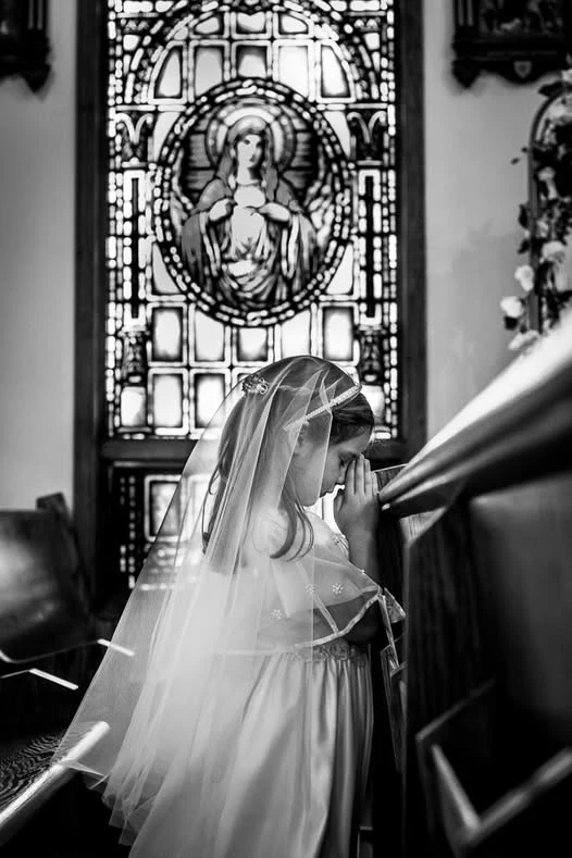 Black and white portrait of a girl in a veil kneeling in a church